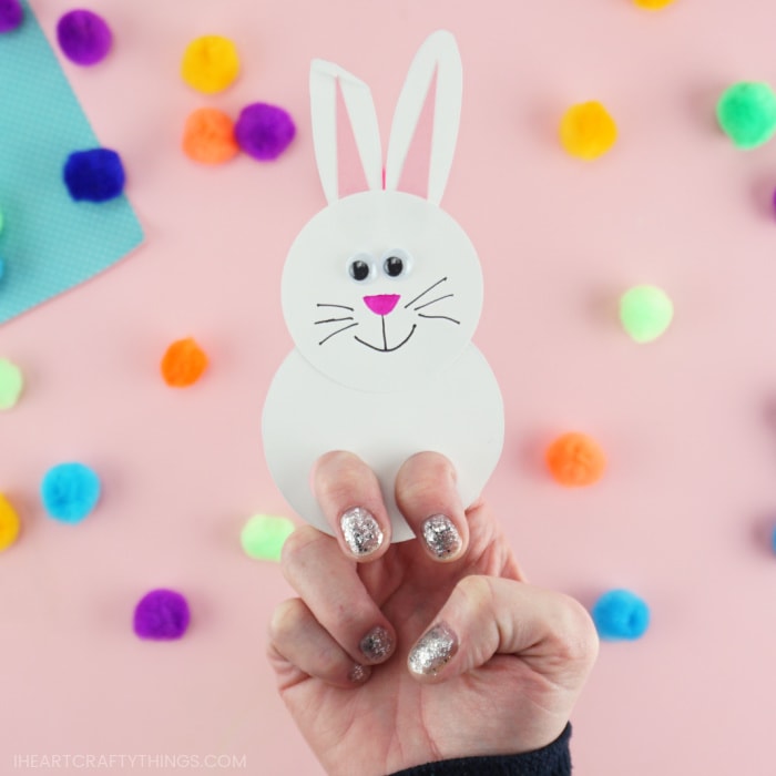 Close up image of a white bunny finger puppet with an adult showing how to place your fingers inside the puppet to play with it.